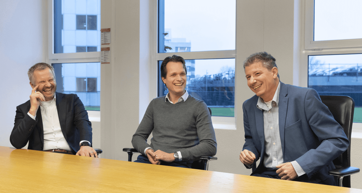 Mannelijke collega's aan een vergadertafel lachen met elkaar.