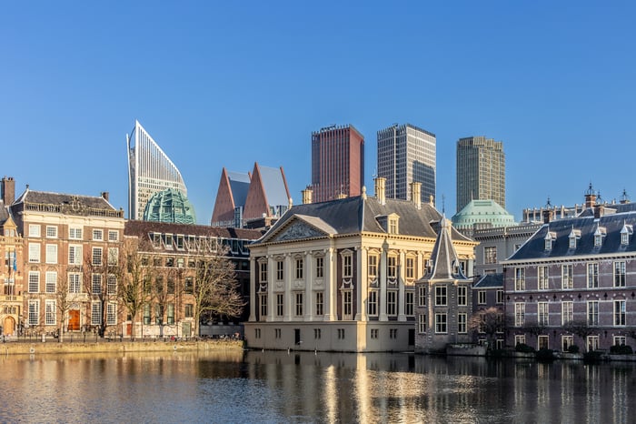 Een panoramisch uitzicht op de skyline van Den Haag, met moderne wolkenkrabbers op de achtergrond en klassieke, historische gebouwen aan de voorgrond, weerspiegeld in het water