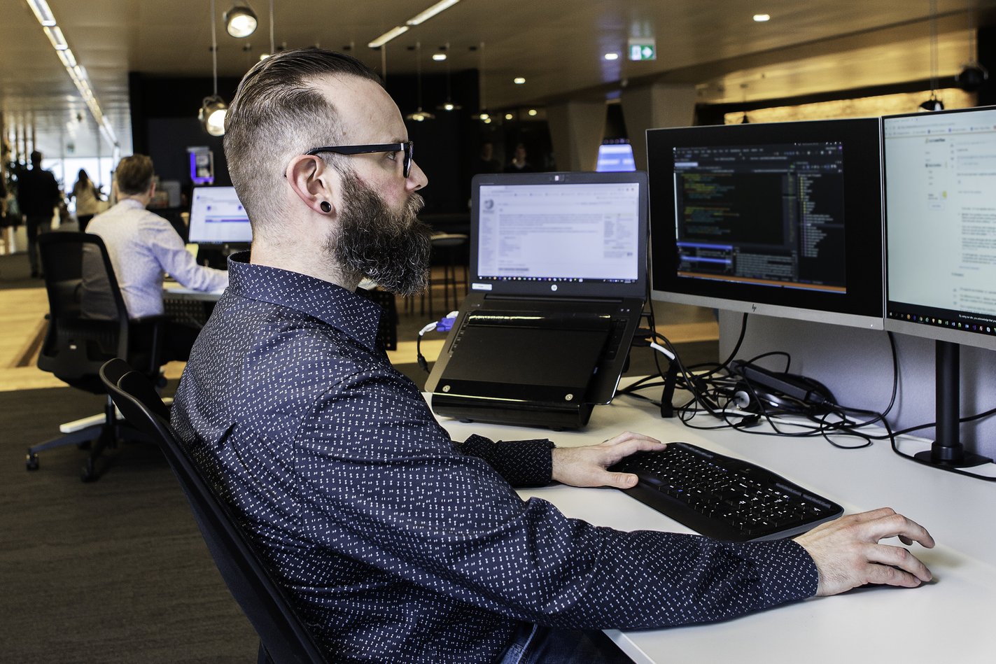 Man werkt achter meerdere computerschermen op een modern kantoor.