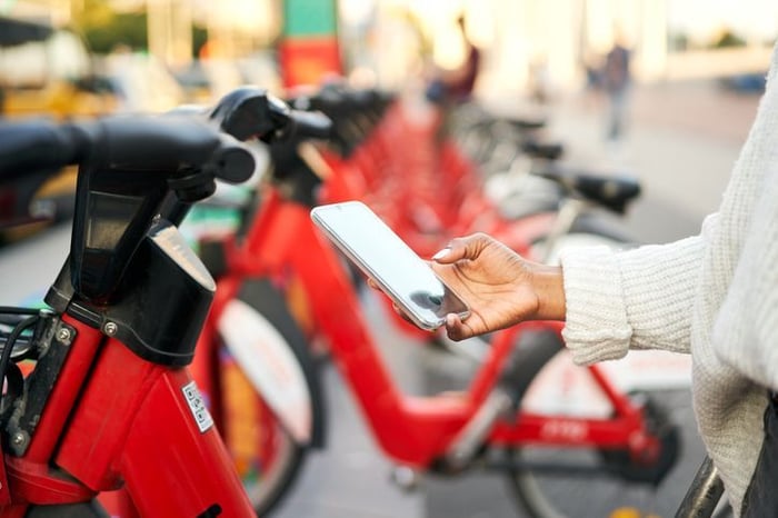 person holding snartphone in hand next to scooters.