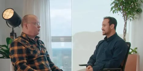 A blond haired man with glasses talking to a dark haired man with a beard