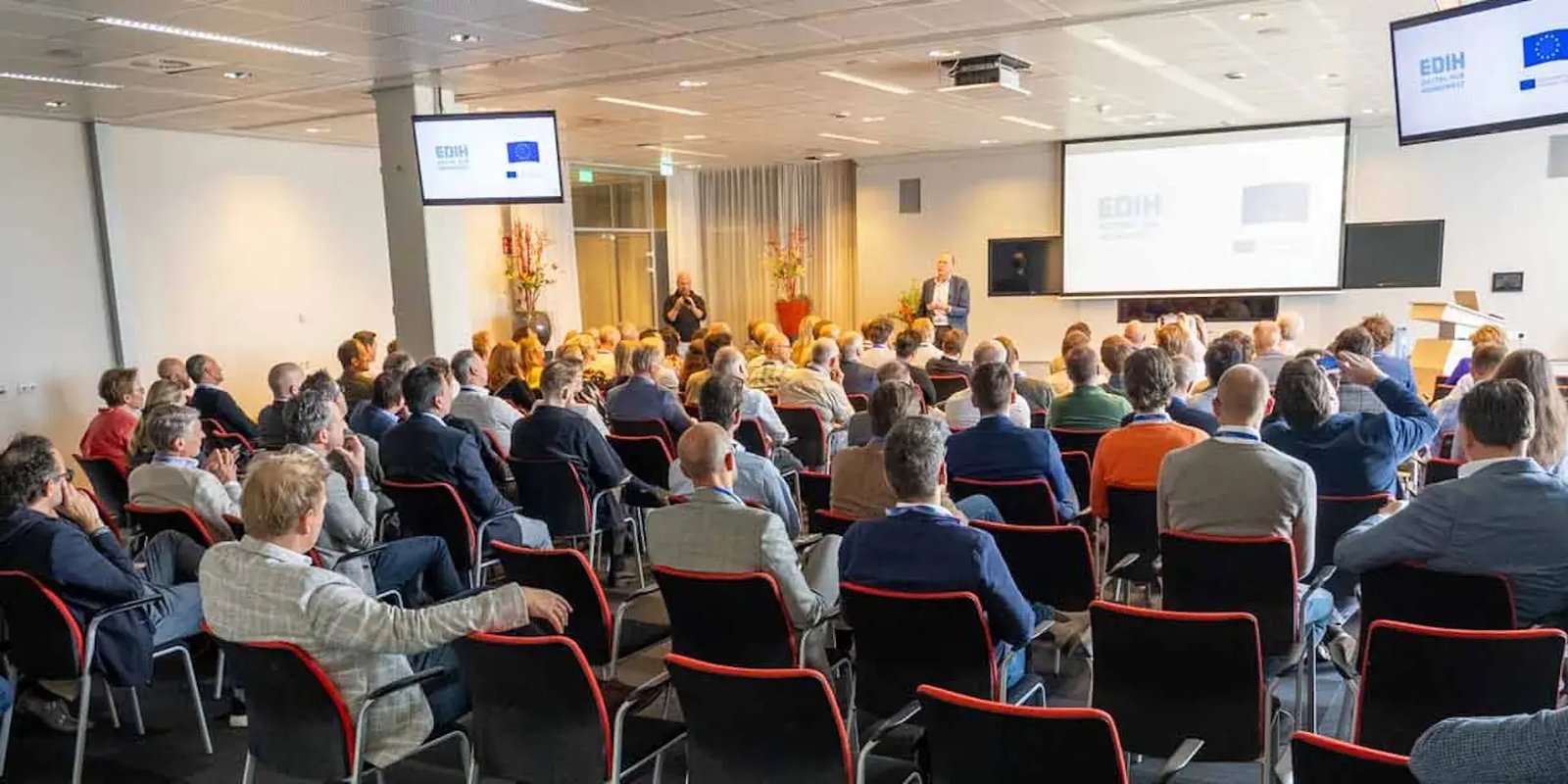 Mensen zitten een een zaal en kijken naar de spreker