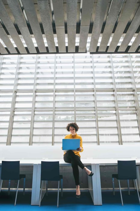 Vrouwelijke werknemer zit in kantoor met haar laptop op schoot.