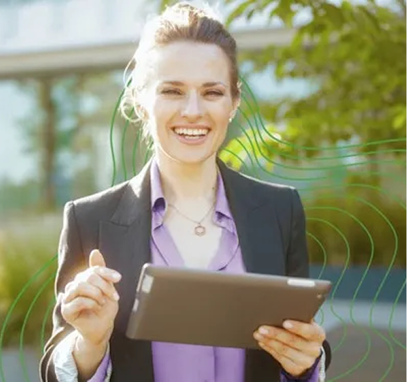 A white lady with dark hair in a ponytail with a purple shirt, smiling in front of the camera with a tablet in her hand.