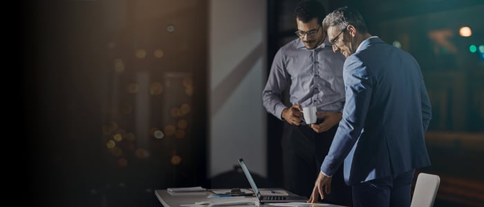 An executive and an employee standing by a laptop