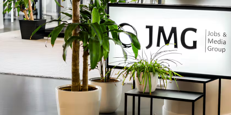 Kantoorinterieur met JMG-logo op een verlicht bord, omringd door groene kamerplanten.