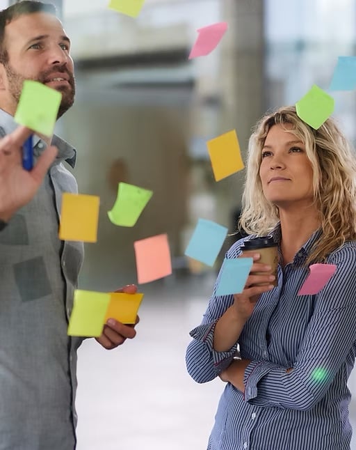 Man en vrouw bekijken kleurrijke post-its op een glazen wand.