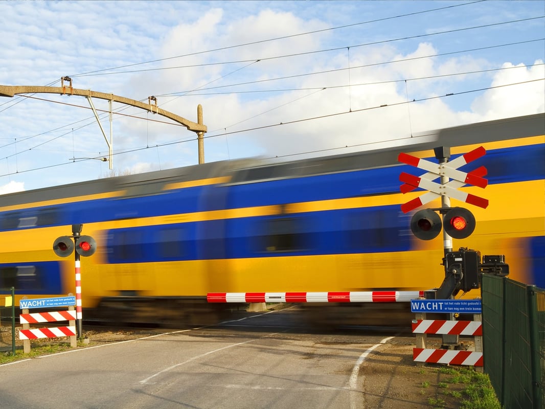 Geel-blauwe NS-trein rijdt over een spoorwegovergang met gesloten slagbomen