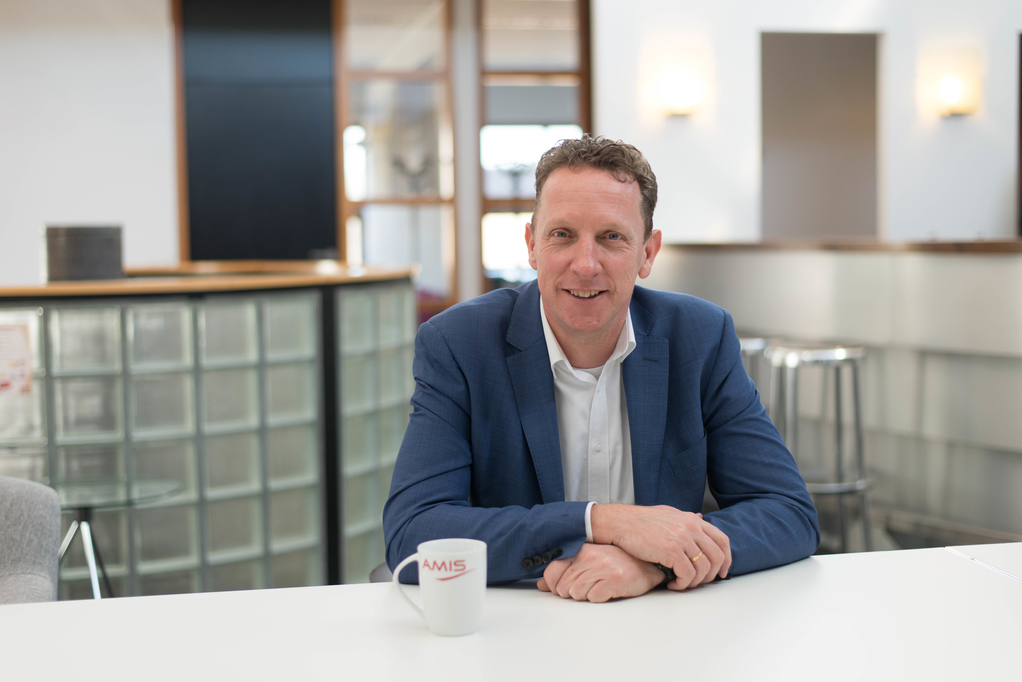 Een man aan tafel die lacht naar de camera