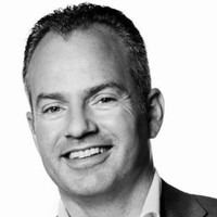 Man glimlacht op een zwart-wit portretfoto.