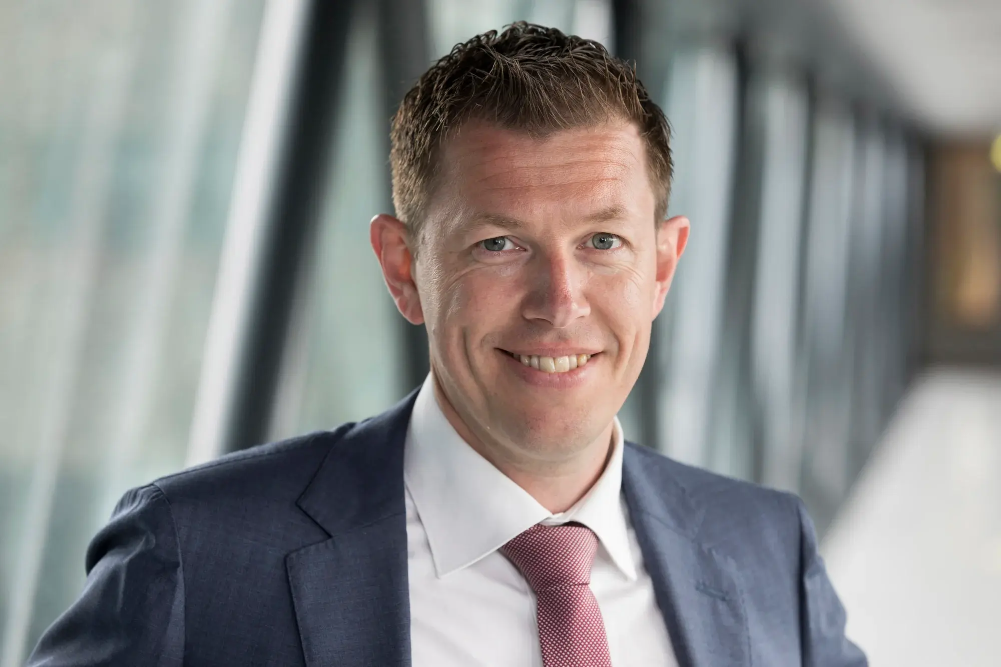 Man in pak met stropdas kijkt lachend de camera in