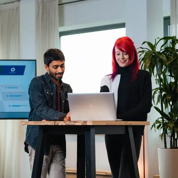 Vrouw met rood haar en man met donker haar bij een laptop aan statafel