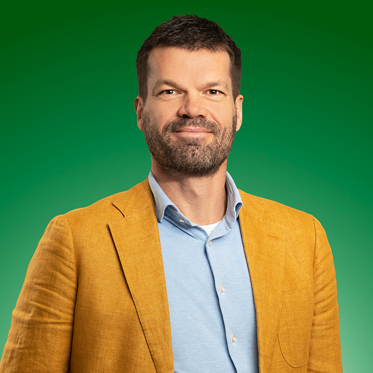 Tjerk Potma in gele blazer en lichtblauw overhemd voor een groene achtergrond.