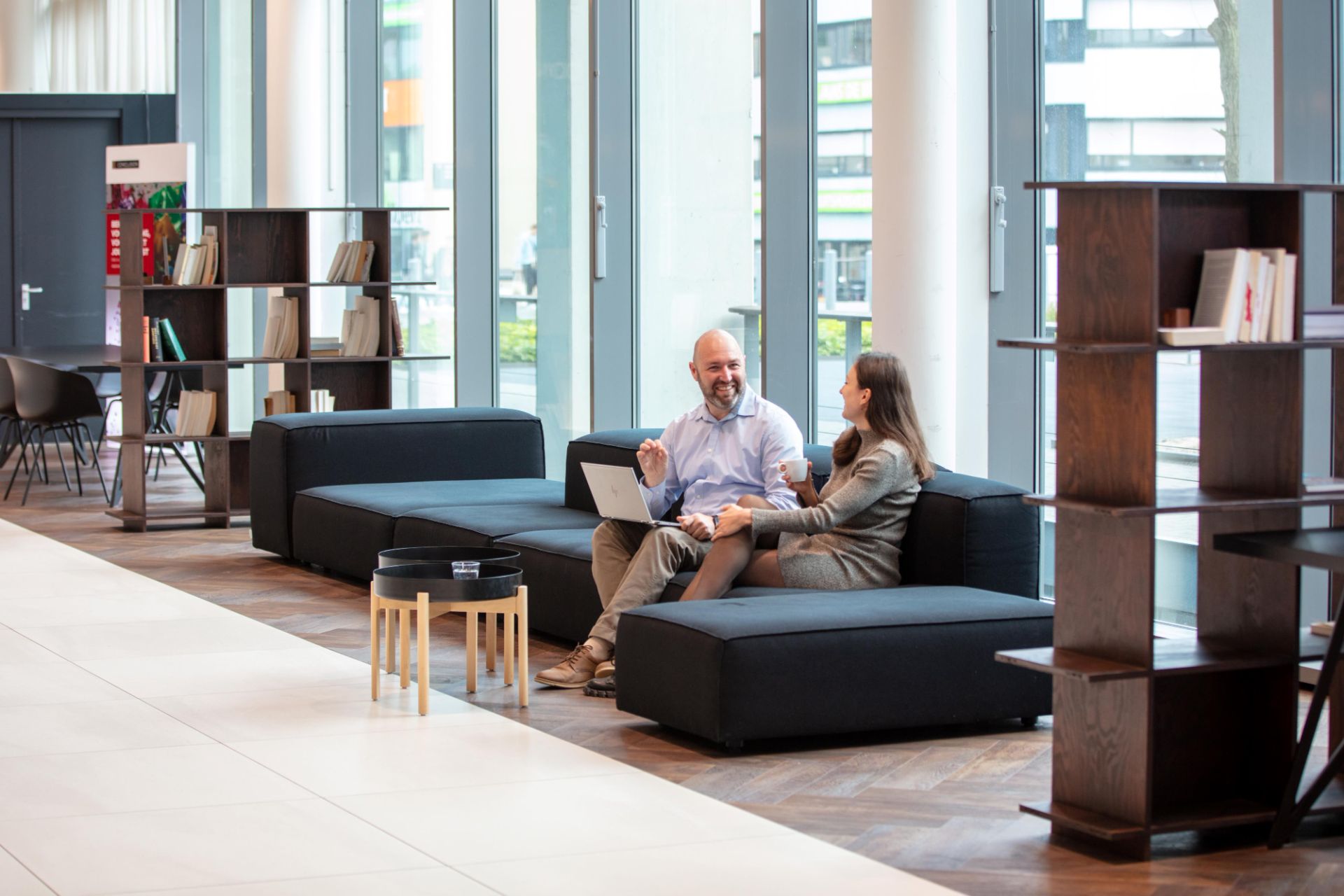 Twee collega's zitten op de bank in de lobby met hun laptop.