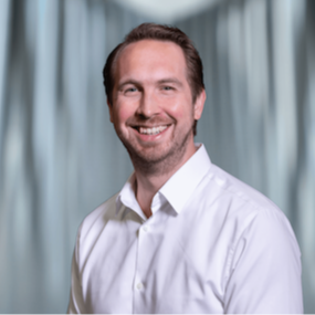 Mannelijke collega kijkt vriendelijk de camera in.