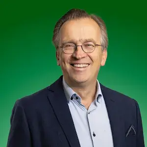 Een man in een blazer glimlacht voor een groene achtergrond.