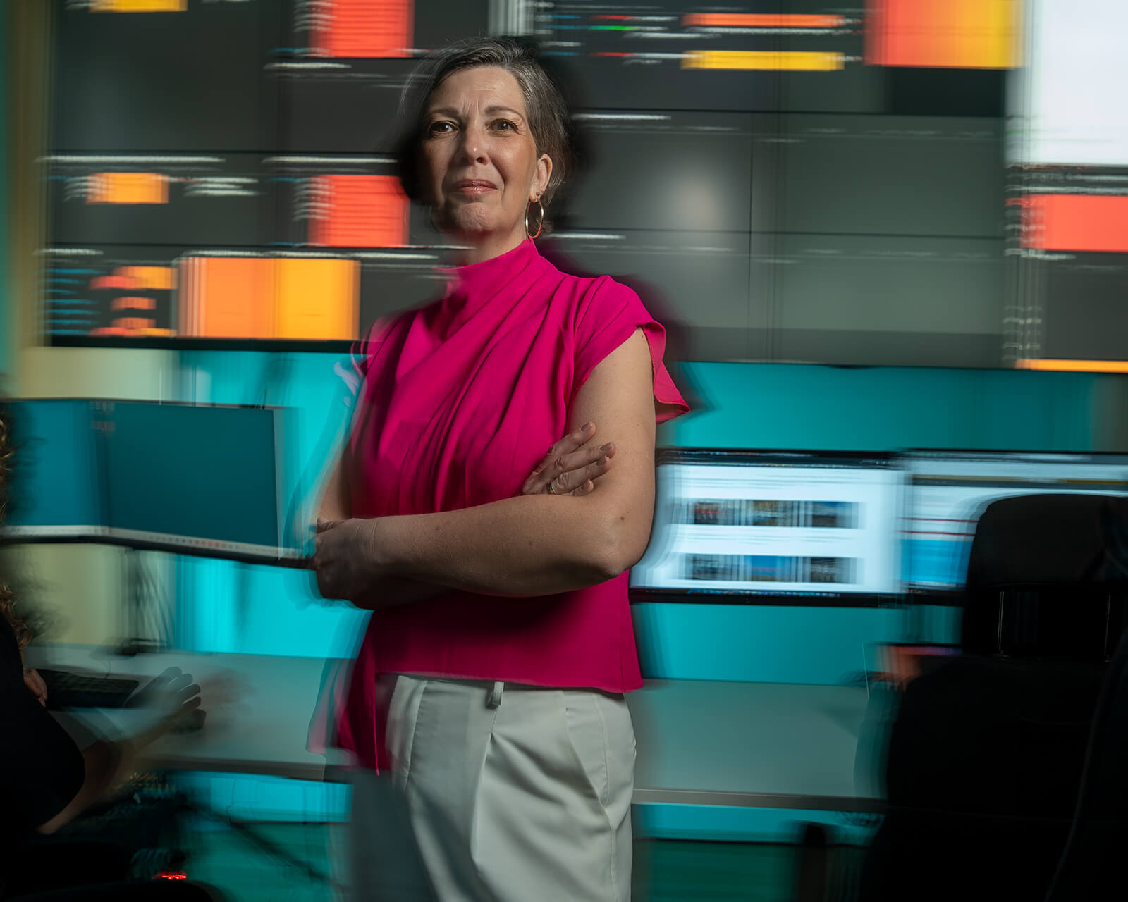 Vrouw kijkt vriendelijk in camera met wazige achtergrond met monitors