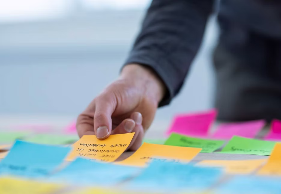 Hand pakt een beschreven post-it van een tafel vol kleurrijke briefjes.